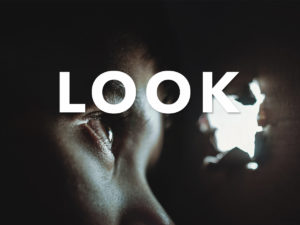 Boy looking through a lit hole in the wall from darkness. The word Look across the image in all caps.