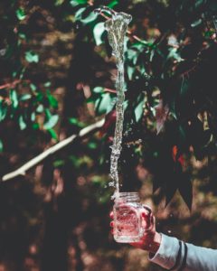 Mason jar in hand catching a stream of water.