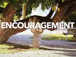 Large tree limb being held up by a huge hand sculpture. It appears the limb may break without the support. The word encouragement is placed over this image.