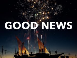 People standing on small sail boats watching fireworks.  The words good news over that image.  