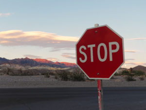 At a stop sign as the sun casts red over rocky mountains