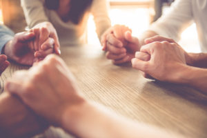 Group of people holding hands and praying at a table. 