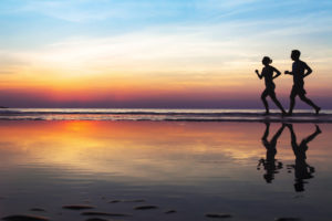 two runners on the beach, silhouette of people jogging at sunset, healthy lifestyle background
