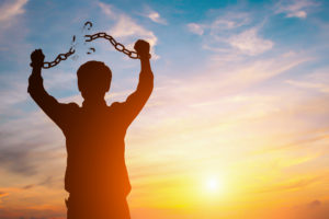 Silhouette image of a man with broken chains in sunset.